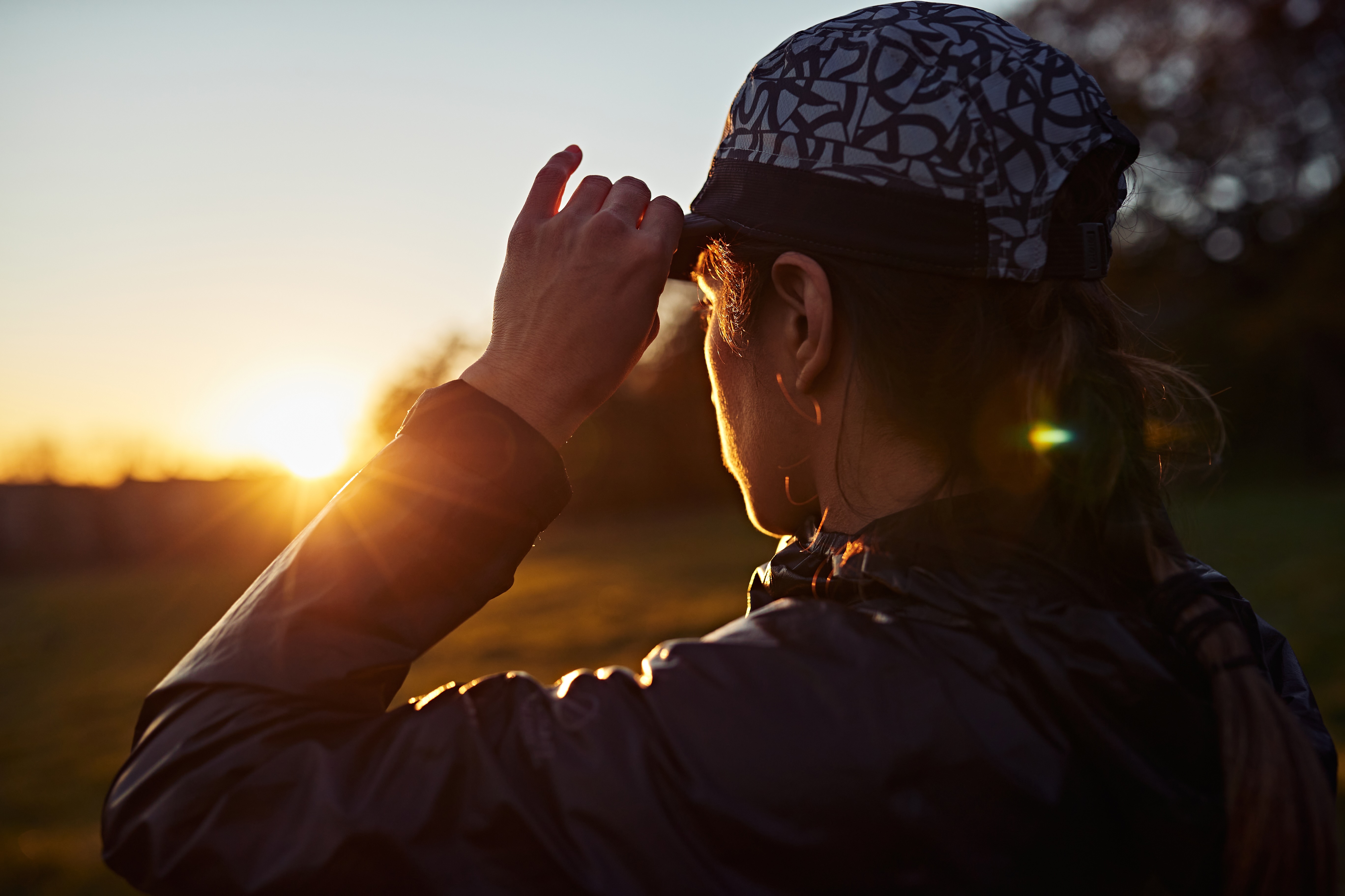 A runner adjusting her cap at sunrise